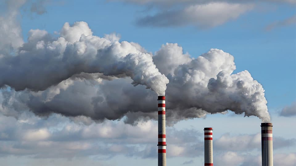 An image of three towers with clouds of emissions coming out the top against a cloudy background